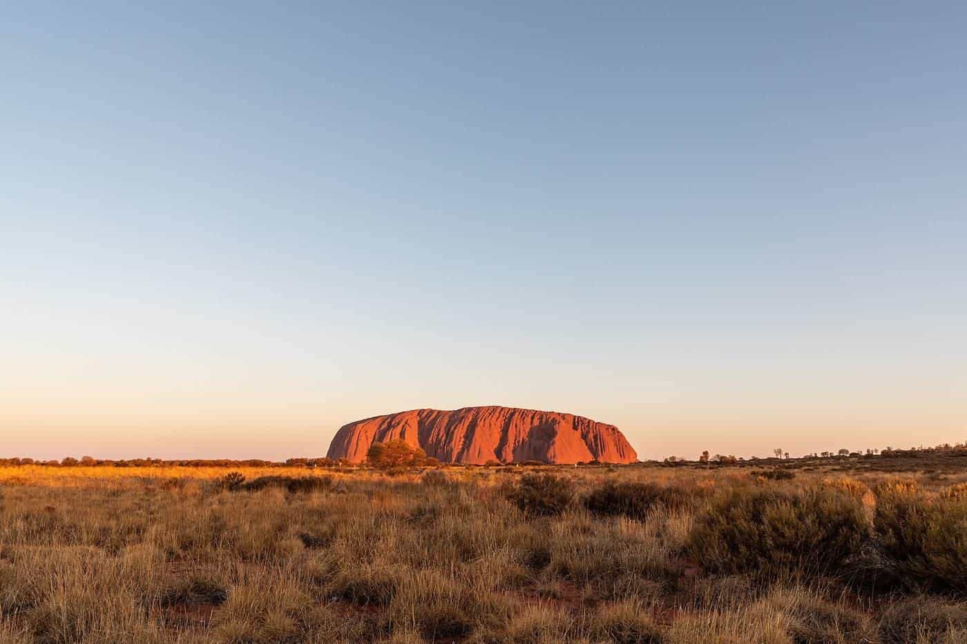 A sunlit red desert landscape near Uluṟu with a clear blue sky